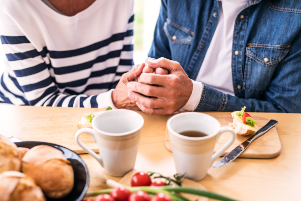 Unrecognizable senior couple eating breakfast at home. An old man and woman sitting at the table, holding hands.