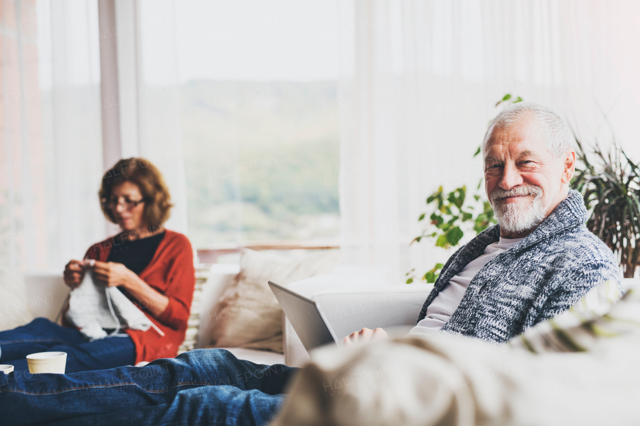 Happy senior couple relaxing at home. A woman knitting and a man using a laptop.