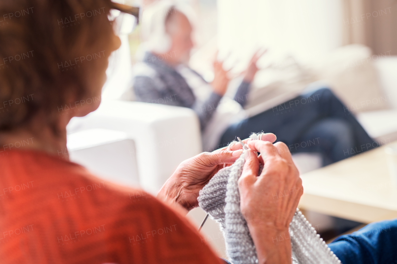 Unrecognizable senior couple relaxing at home. A woman knitting, and man listening to music in the background.