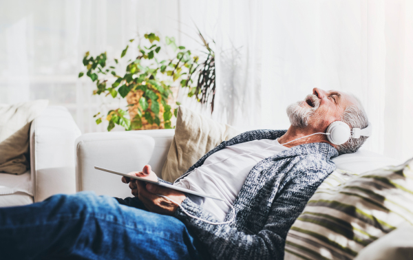 Senior man with tablet relaxing at home. Old man listening to music.