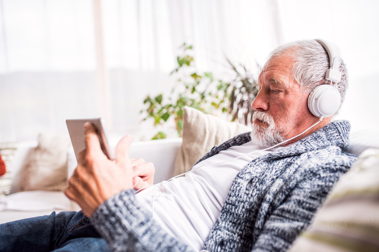 Senior man with tablet and headpones relaxing at home. Old man listening to music.