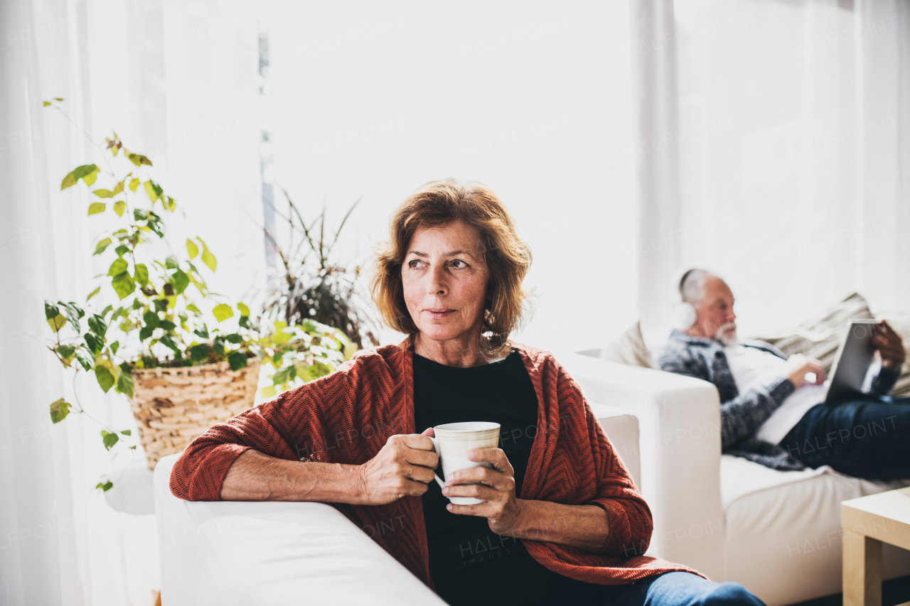 Happy senior couple relaxing at home. A woman holding a cup and a man with tablet listening to music.