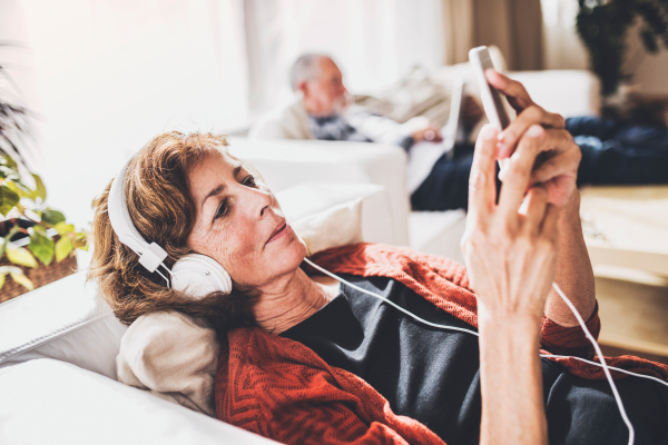 Happy senior couple relaxing at home. A woman with smartphone and headphones listening to music.