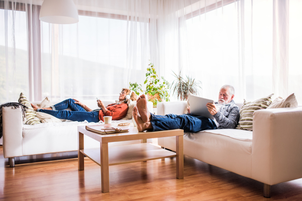 Happy senior couple with tablet and smartphone relaxing at home.