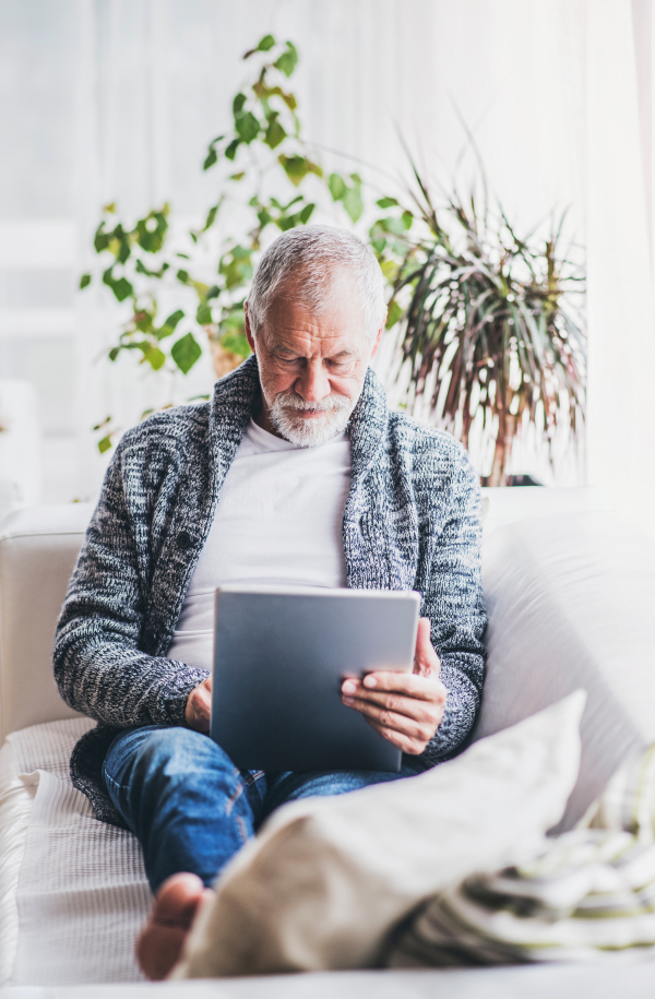 Happy senior man with tablet relaxing at home.