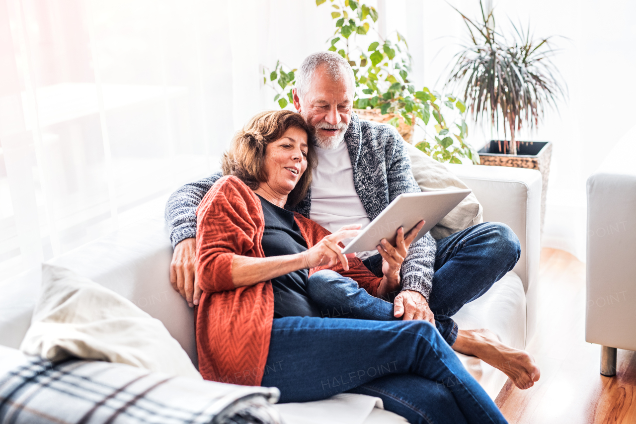 Happy senior couple with tablet relaxing at home.