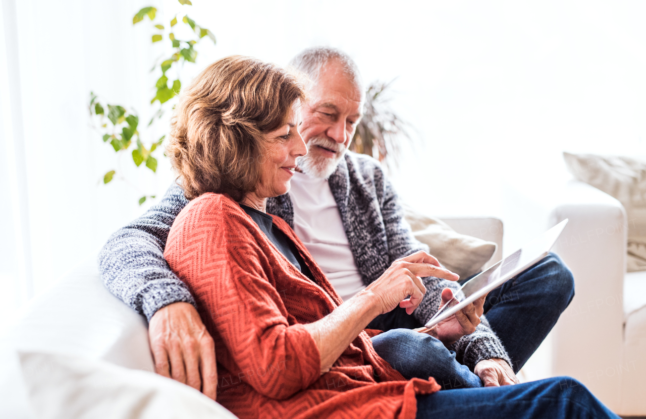 Happy senior couple with tablet relaxing at home.