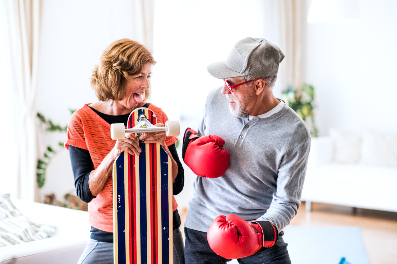 Crazy senior couple with boxing gloves and longboard having fun at home.