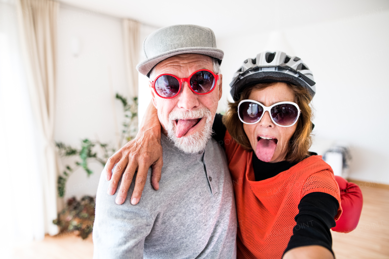 A crazy senior couple with sunglasses having fun at home, sticking a tongue out.