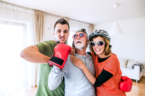 A crazy senior couple with grandson having fun at home, sticking a tongue out.