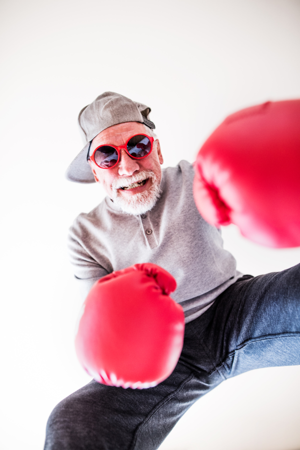 A crazy senior man with red sunglasses and boxing gloves having fun at home.