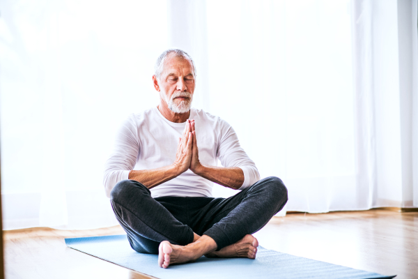 Active senior man meditating at home, eyes closed.