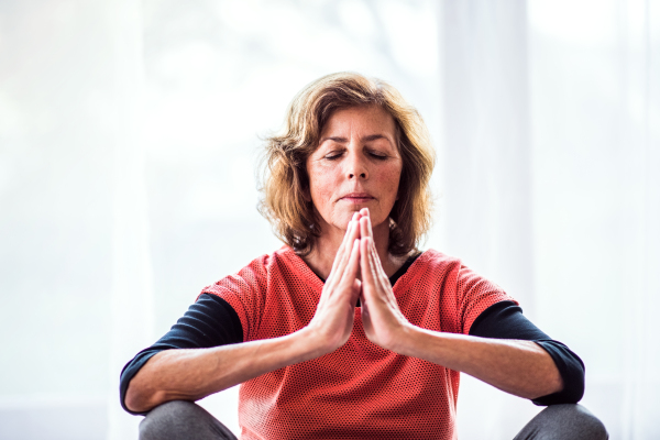 Active senior woman meditating at home, eyes closed.