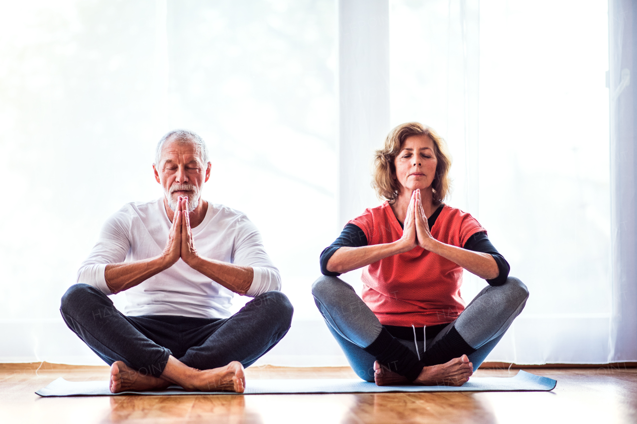 Active senior couple meditating at home, eyes closed.