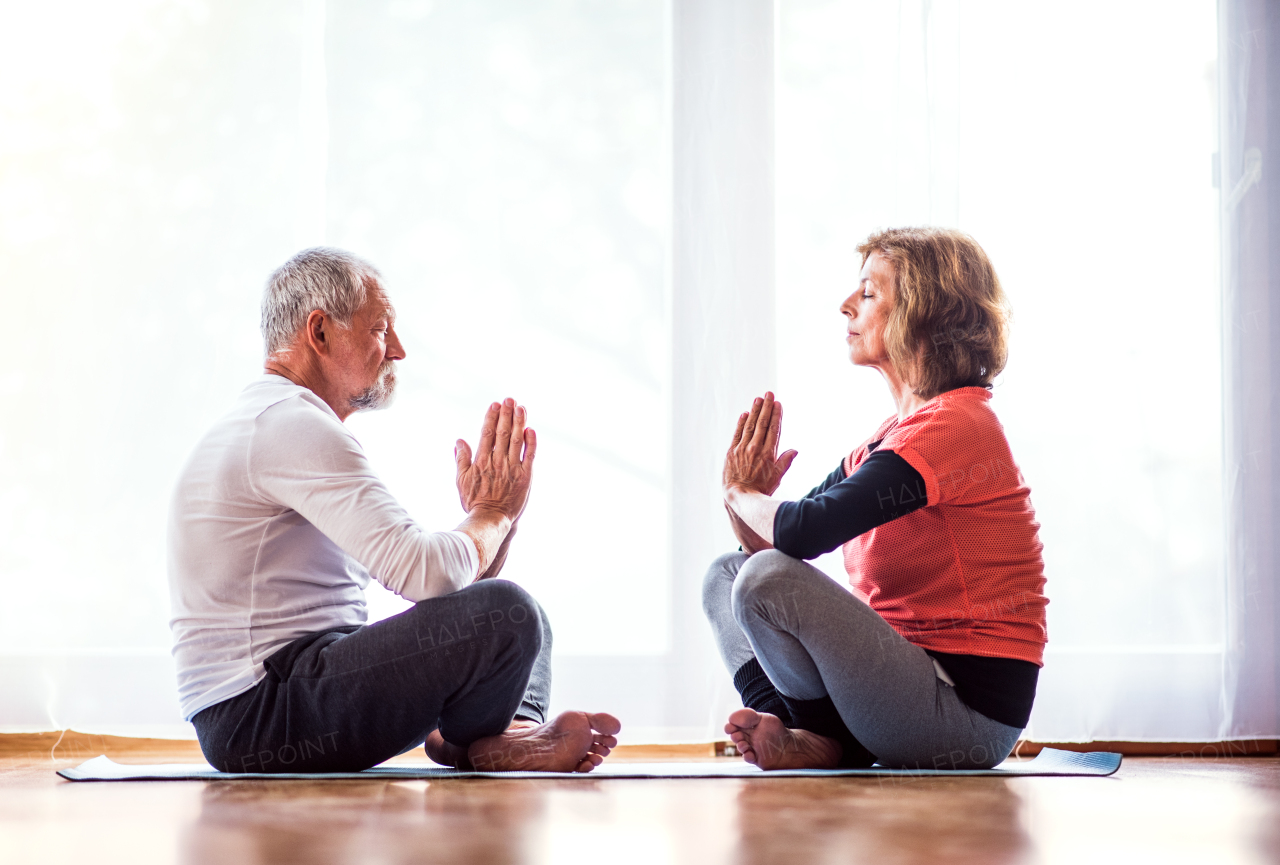 Active senior couple meditating at home, eyes closed.