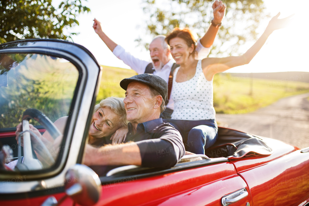 A group of elderly friends and retro car, veteran on a roadtrip through countryside, having fun together. Retired seniors enjoying free time and retirement.