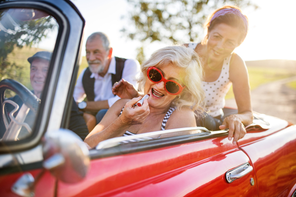 A group of elderly friends and retro car, veteran on a roadtrip through countryside, having fun together. Retired seniors enjoying free time and retirement.