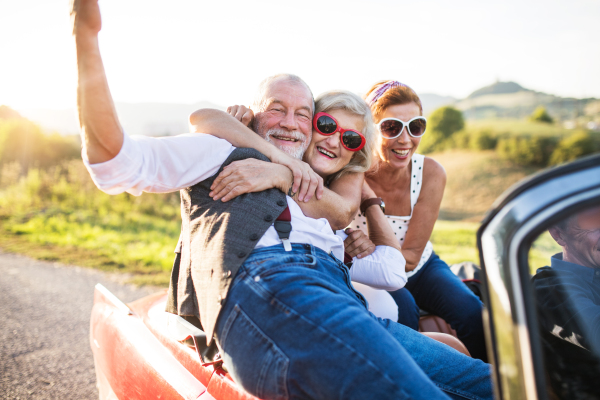 A group of elderly friends and retro car, veteran on a roadtrip through countryside, having fun together. Retired seniors enjoying free time and retirement.