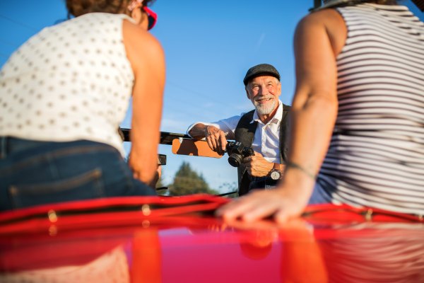 A group of elderly friends and retro car, veteran on a roadtrip through countryside, having fun together. Retired seniors enjoying free time and retirement.