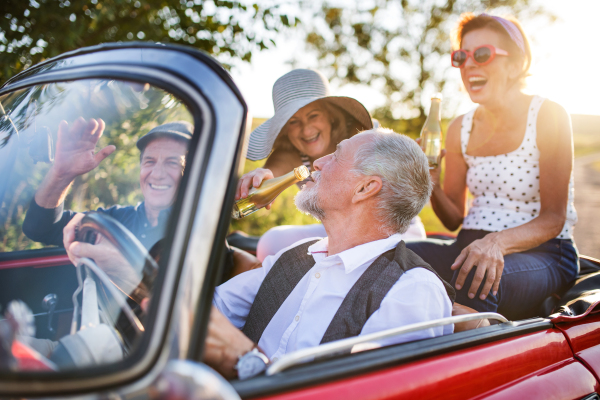 A group of elderly friends and retro car, veteran on a roadtrip through countryside, having fun together. Retired seniors enjoying free time and retirement.