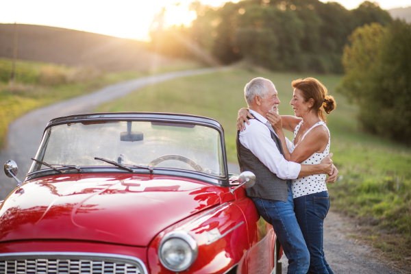 A group of elderly friends and retro car, veteran on a roadtrip through countryside, having fun together. Retired seniors enjoying free time and retirement.