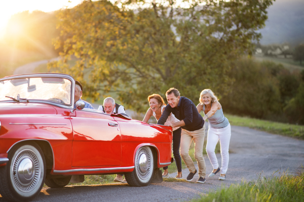 A group of elderly friends and retro car, veteran on a roadtrip through countryside, having fun together. Retired seniors enjoying free time and retirement.