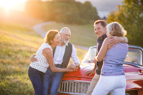 A group of elderly friends and retro car, veteran on a roadtrip through countryside, having fun together. Retired seniors enjoying free time and retirement.