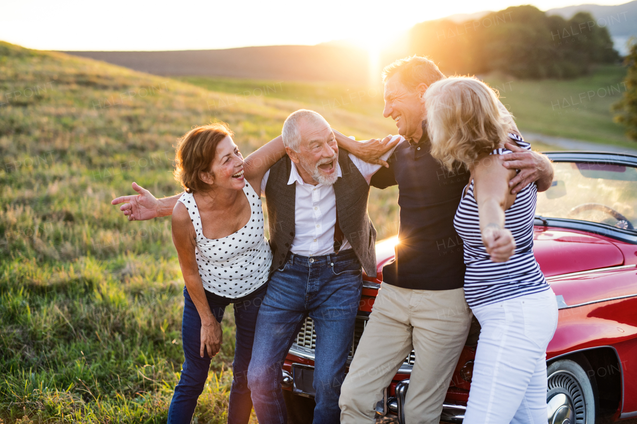 A group of elderly friends and retro car, veteran on a roadtrip through countryside, having fun together. Retired seniors enjoying free time and retirement.