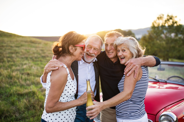 A group of elderly friends and retro car, veteran on a roadtrip through countryside, having fun together. Retired seniors enjoying free time and retirement.