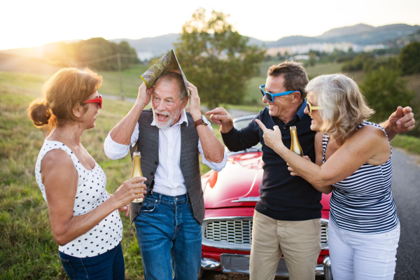 A group of elderly friends and retro car, veteran on a roadtrip through countryside, having fun together. Retired seniors enjoying free time and retirement.