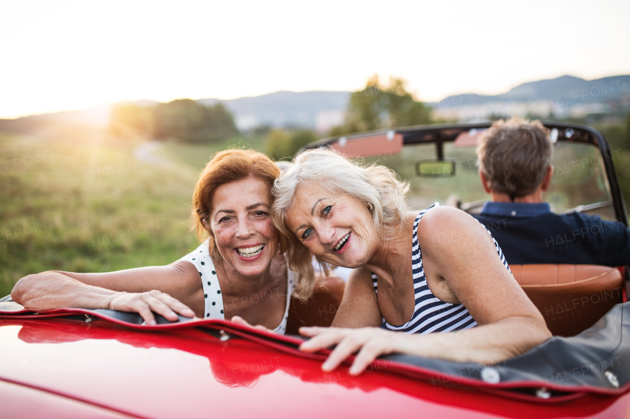 A group of elderly friends and retro car, veteran on a roadtrip through countryside, having fun together. Retired seniors enjoying free time and retirement.