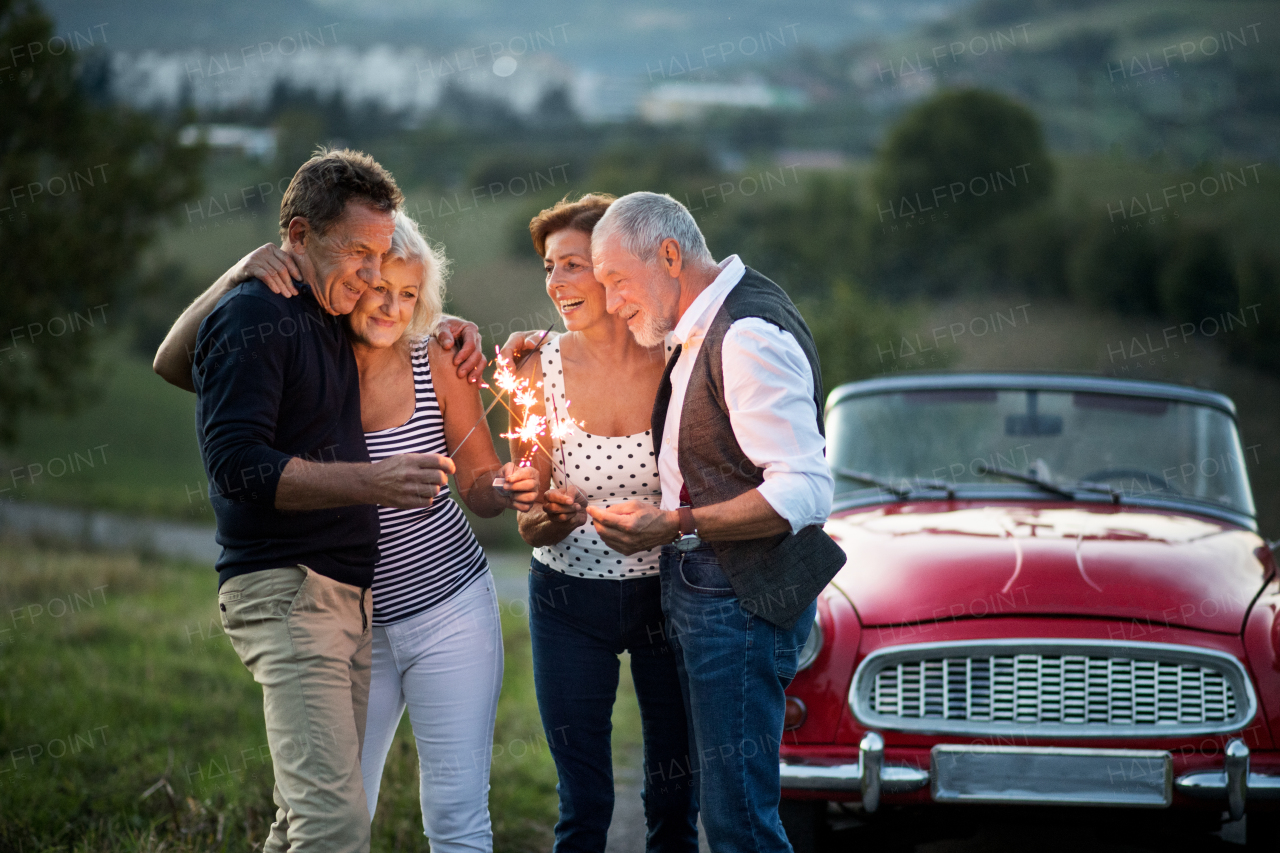 A group of elderly friends and retro car, veteran on a roadtrip through countryside, having fun together. Retired seniors enjoying free time and retirement.