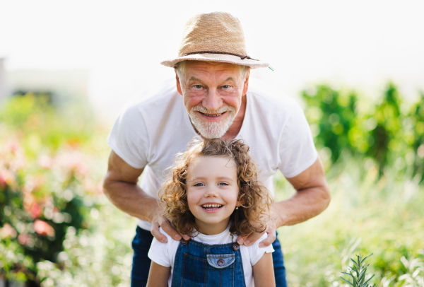 Portrait of small girl with senior grandfather in the backyard garden, standing and looking at camera.