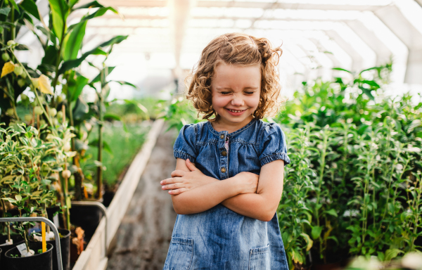 A portrait of small girl standing in the greenhouse, grimacing.