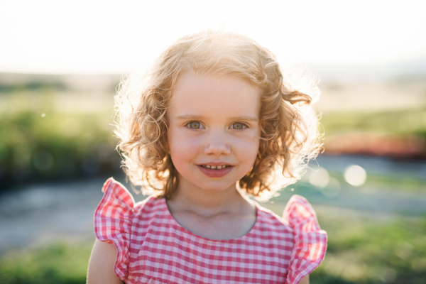 Portrait of cute small girl standing in the backyard garden, looking at camera.