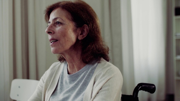 A senior woman in wheechair sitting at the table at home, talking to somebody.