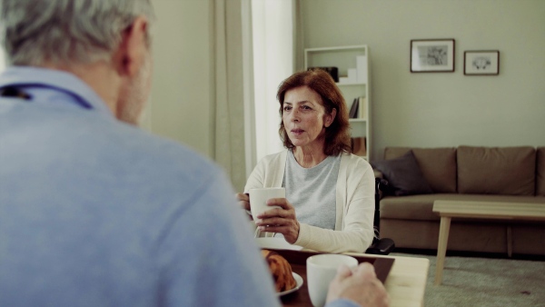 A senior couple with coffee sitting at the table at home, having breakfast and talking.