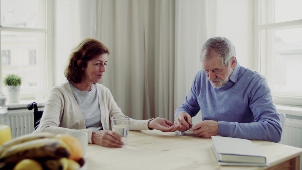 A senior couple with wheelchair sitting at the table at home, taking drugs and pills.