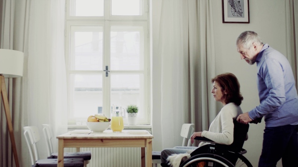 A senior couple in the morning at home, a man helping his disabled wife.