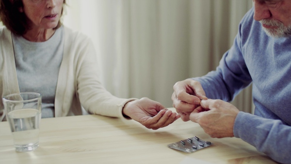 A midsection of unrecognizable senior couple sitting at the table at home, taking drugs and pills.