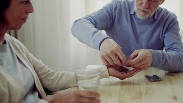 A senior couple with wheelchair sitting at the table at home, taking drugs and pills.