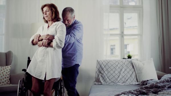 A caring senior man lifting disabled wife from wheelchair and putting her in bed.