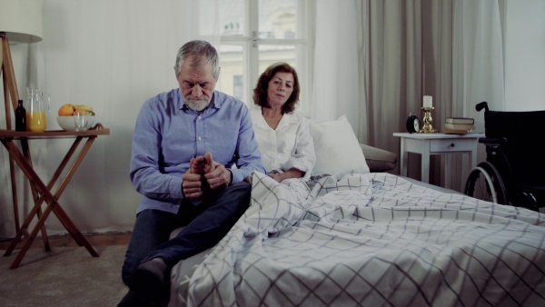 A senior couple sitting on bed at home, a man giving feet massage to his ill wife.