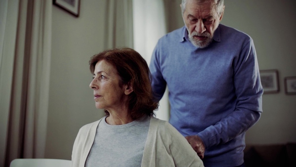 A senior couple at the table at home, a man helping his disabled wife. Slow motion.