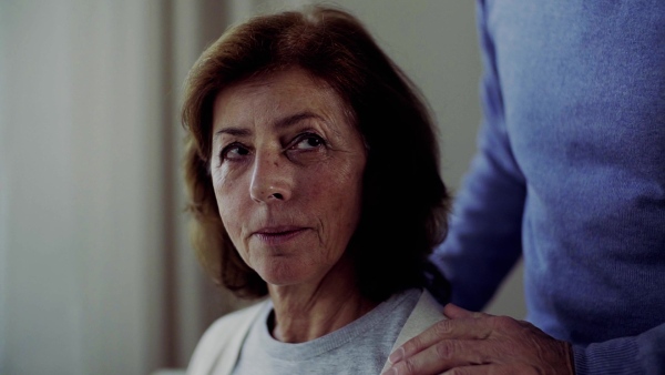 A close-up of loving and caring senior man talking to his disabled wife at home. Slow motion.