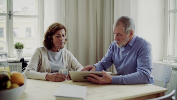 Happy senior couple with wheelchair and tablet sitting at the table at home, talking. Slow motion.