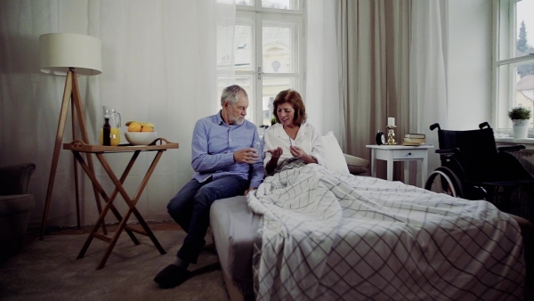 A senior couple sitting on bed at home, a man giving medication to his ill wife. Slow motion.