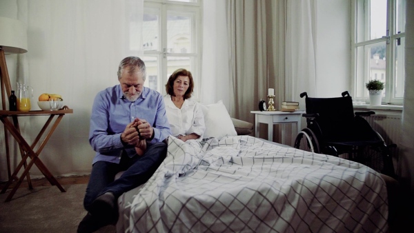 A senior man and his sad disabled wife sitting on bed, giving a foot massage. Slow motion.