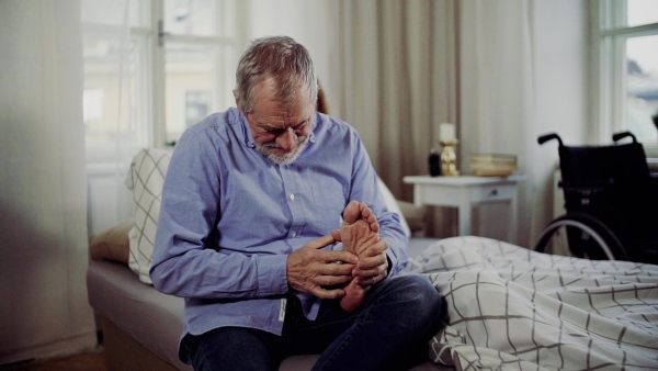 A senior man and his sad disabled wife sitting on bed, giving a foot massage. Slow motion.