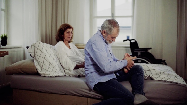 A senior man and his sad disabled wife sitting on bed, giving a foot massage. Slow motion.